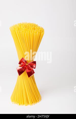 Un mazzo verticale, un mazzo di spaghetti crudi legati con una corda con un arco rosso. Fascio su sfondo bianco. Il concetto di cucina italiana per le vacanze. Foto Stock