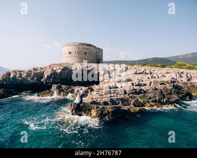 Sposa e sposo si erigono sulle rocce sullo sfondo della fortezza di Arza Foto Stock
