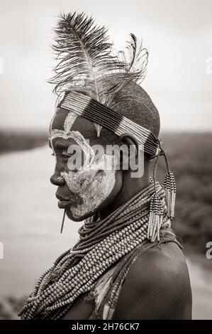 Donna del Karo Tribe con un volto dipinto e piume per la decorazione vicino al fiume Foto Stock