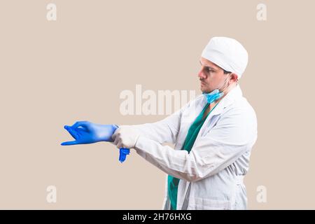 Giovane medico in tuta bianca e maschera protettiva per la respirazione mette i guanti sulle mani su sfondo giallo isolato. Foto Stock