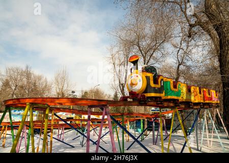 Un treno per bambini corre su alte rotaie sopra le nevi tra gli alberi in un parco divertimenti cittadino. Foto Stock