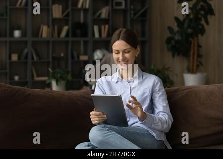 Bella giovane donna seduta sul divano utilizzando il tablet digitale Foto Stock