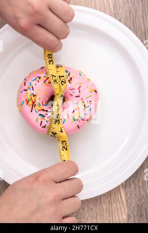 Primo piano di ciambella e nastro di misurazione, perdita di peso e dieta concetto. Foto Stock