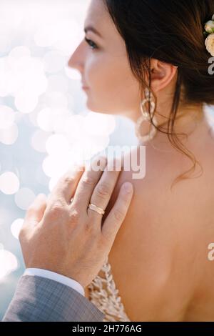 Sposi la mano con un anello sul suo dito giace sulla spalla della sposa in un abito bianco. Verticale Foto Stock