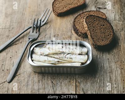 le sardine aperte possono forchette e fette di pane su un vecchio tavolo da cucina in legno Foto Stock