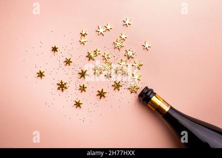 Bottiglia di champagne con spruzzi dorati scintillanti su sfondo rosa. Disposizione piatta, vista dall'alto, stile natalizio alla moda. Foto Stock