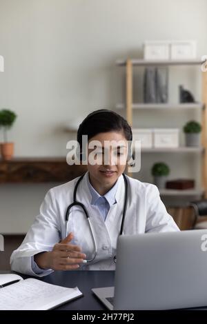 Foto verticale medico indiano in cuffie parlare, utilizzando il computer portatile Foto Stock