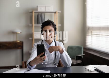 Sorridente medico indiano in cuffie utilizzando smartphone, parlando Foto Stock