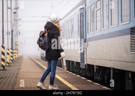 Viaggio in treno. Donna con zaino a bordo per allenarsi alla stazione ferroviaria in nebbia mattina. Trasporto ferroviario Foto Stock