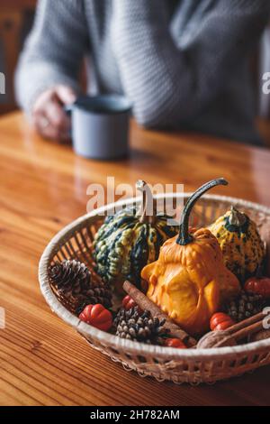 Decorazione autunnale con zucche su tavola di legno. Donna defocused che indossa un maglione a maglia gustando una bevanda a base di caffè Foto Stock