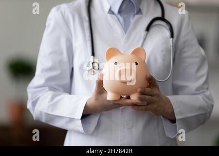 Crop close up medico femmina tenendo rosa Piggy banca Foto Stock