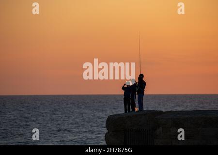 Tramonto mediterraneo fotografato alla silhouette di Acre Israel di pesca ragazzi locali Foto Stock