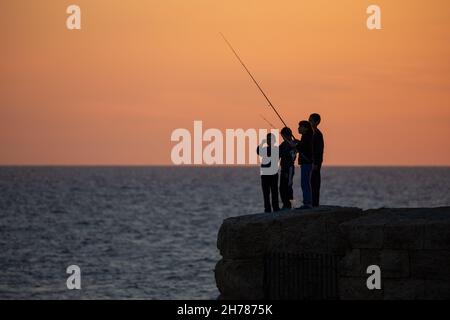 Tramonto mediterraneo fotografato alla silhouette di Acre Israel di pesca ragazzi locali Foto Stock