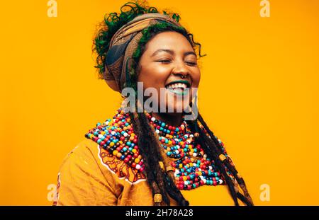 Ragazza spensierata che indossa abiti tradizionali. Giovane donna alla moda sorridente con gli occhi chiusi mentre si alza su uno sfondo giallo. St Foto Stock