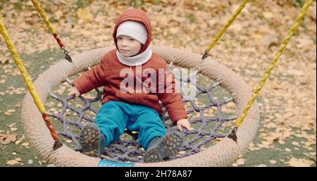 Piccolo, carino bambino corre su un swing nel cortile su una passeggiata Foto Stock