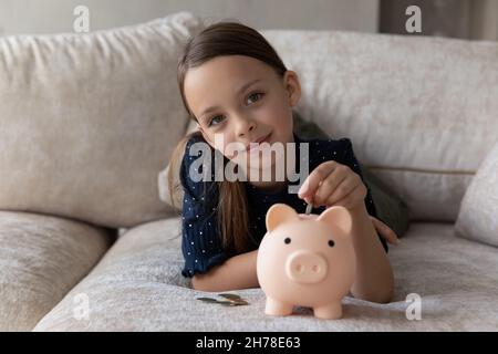 Carina ragazza piccola fruccia mettere la moneta in banca Piggy Foto Stock