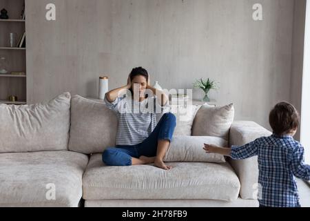 Ragazzo disobbediente che corre in soggiorno e disturba la madre Foto Stock