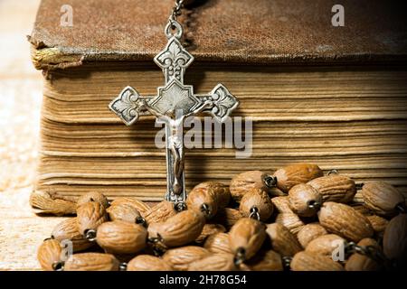 Particolare di un antico crocifisso d'argento e rosario con perle di legno. Su un tavolo di legno con una vecchia Sacra Bibbia Foto Stock