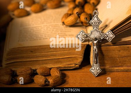 Crocifisso d'argento e rosario con perle di legno su una vecchia Bibbia Santa su un tavolo di legno con ombre scure Foto Stock