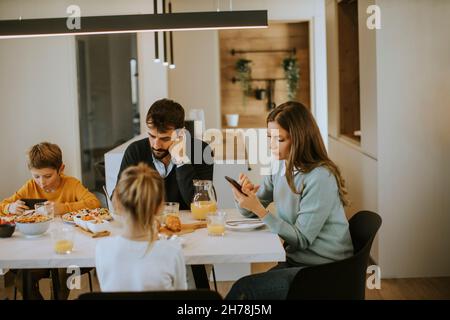 La famiglia usa i telefoni cellulari mentre consumata la colazione al tavolo da pranzo dell'appartamento Foto Stock