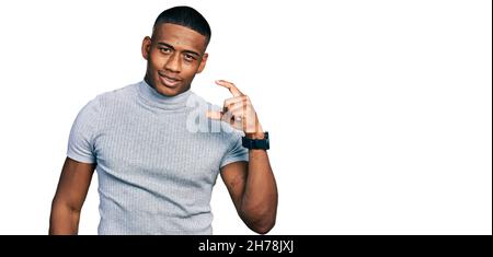 Giovane uomo nero con t shirt casual sorridente e sicuro gesturing con mano facendo piccolo segno con le dita guardando e la fotocamera. Misurare co Foto Stock