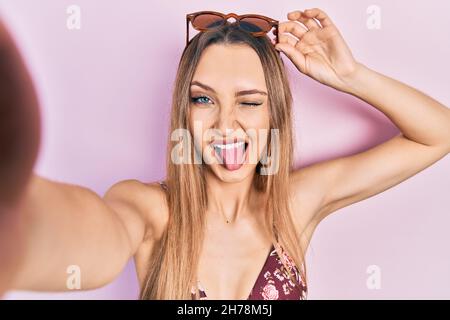 Giovane ragazza bionda che indossa bikini prendendo un selfie che attacca la lingua felice con espressione divertente. Foto Stock