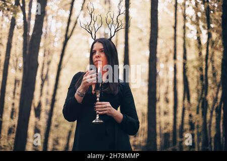 Scatto di donna misteriosa in abito nero che tiene candela su candelabro nelle sue mani che esegue rituale magico nella foresta scura autunno. Concetto di stregoneria Foto Stock