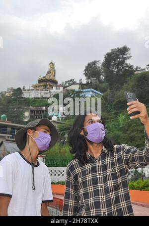Due amici maschi con maschera che indossa il viso prendendo selfie insieme all'esterno durante covid-19 pandemia Foto Stock