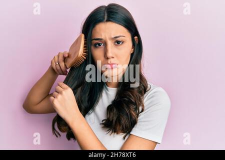 Giovane ispanica donna styling capelli con pettine depresso e preoccuparsi per la sofferenza, piangendo arrabbiato e paura. Espressione triste. Foto Stock