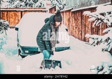 donna con pala che pulisce la neve intorno all'auto. Pala invernale. Rimuovere la neve dopo la bizzarda Foto Stock