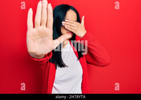 Bella donna ispanica con piercing naso indossando look casual e occhiali che coprono gli occhi con le mani e facendo stop gesture con expressi triste e paura Foto Stock