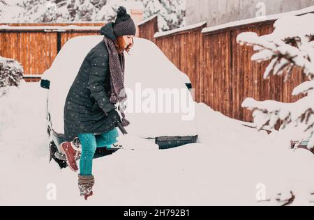 donna con pala che pulisce la neve intorno all'auto. Pala invernale. Rimuovere la neve dopo la bizzarda Foto Stock