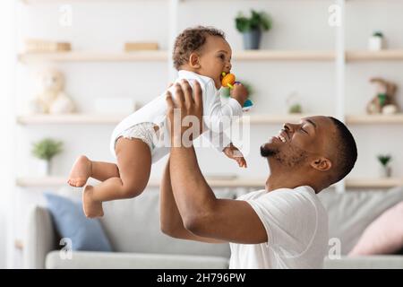 Rapporto del bambino del Padre. Happy Black Man che solleva il suo adorabile Figlio infantile Foto Stock