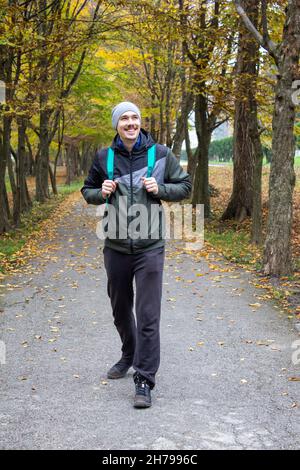 Ritratto di un giovane uomo vagabondo sorridente con zaino va sulla strada felice escursionista camminare solitario Foto Stock