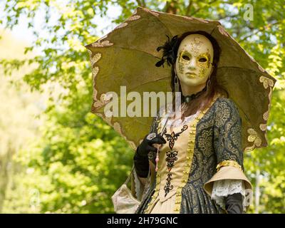 Donna in costume e maschera al carnevale veneziano con ombrello dorato. Blu cielo e gli alberi sullo sfondo. Foto Stock