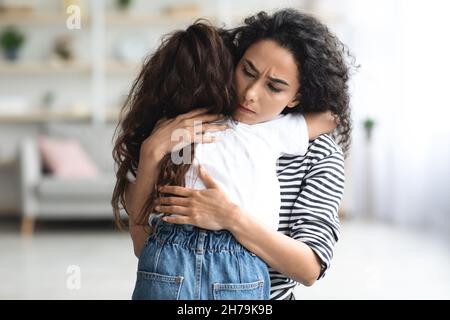 Madre mediorientale dai capelli lunghi che confortava la sua figlia piangente triste Foto Stock