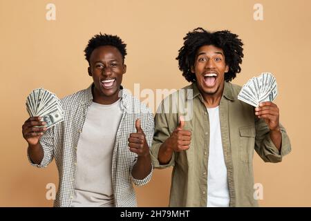 Grande successo. Due eccitati Black Guys che Hold Cash e che mostrano le Thumbs in alto Foto Stock