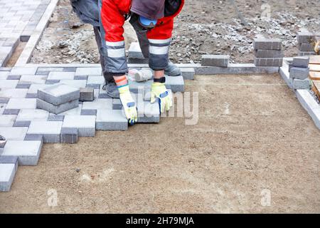 Un operatore che indossa guanti protettivi deposita con cura lastre di pavimentazione lungo un filo allungato su un'area sabbiosa piana preparata. Spazio di copia. Foto Stock