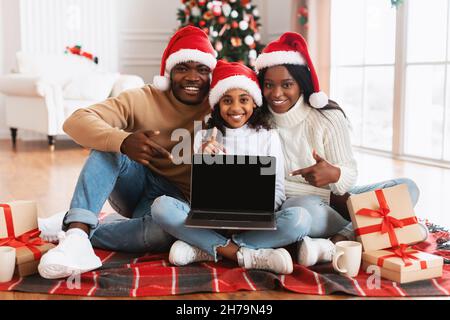Felice famiglia nero festivo che mostra notebook con schermo vuoto, mockup Foto Stock
