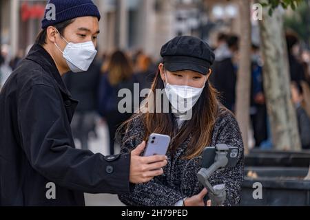 Barcellona, Spagna. 21 Nov 2021. Una giovane coppia turistica asiatica che indossa maschere protettive è visto con i loro dispositivi mobili nella zona commerciale di Portal d'Angel.nonostante l'aumento delle infezioni di Covid-19 in Europa, l'uso di maschere è ancora volontario a Barcellona, Mentre la nazione attende nuove misure sanitarie restrittive di fronte a una nuova ondata di infezioni del Covid-19. (Foto di Paco Freire/SOPA Images/Sipa USA) Credit: Sipa USA/Alamy Live News Foto Stock