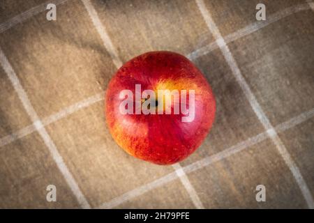Un'allettante mela d'autunno rossa con una tinta gialla dall'alto. Asciugamano in lino sullo sfondo, marrone chiaro con quadrati bianchi. Una fotografia di un sano l Foto Stock