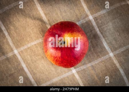 Un'allettante mela d'autunno rossa con una tinta gialla dall'alto. Asciugamano in lino sullo sfondo, marrone chiaro con quadrati bianchi. Una fotografia di un sano l Foto Stock