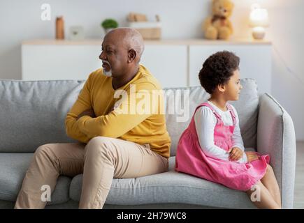 Offeso afroamericano bambino piccolo e uomo maturo si ignorano a vicenda dopo litigare sul divano in soggiorno Foto Stock