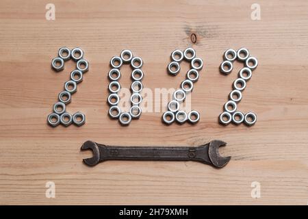 I numeri del nuovo anno 2022 sono rivestiti con dadi metallici su un tavolo in legno ed enfatizzati con una chiave. Vista dall'alto. Foto Stock