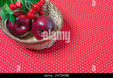 Mele rosse e bacche rosse in un cestino di vimini. Foto Stock
