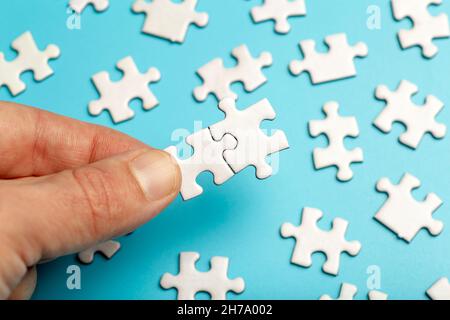 I pezzi di puzzle sono collegati. Pezzi di puzzle bianchi in mano su sfondo blu. Business, partner, soluzione, alleanza, concetto di Unione. Foto di alta qualità Foto Stock