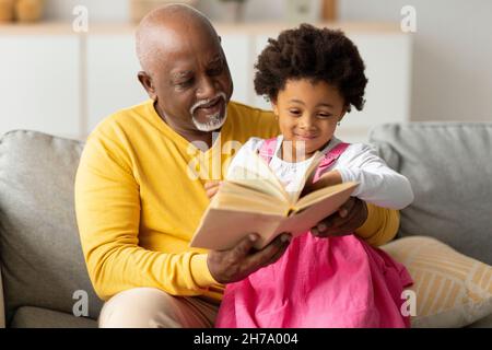 Allegro carino afroamericano piccola nonna e grande nonno libro lettura con fiabe sul divano Foto Stock