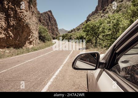 Vista dall'auto sul lato della strada verso lo specchietto retrovisore e la tortuosa strada di montagna Foto Stock