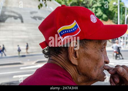 Caracas, Miranda, Venezuela. 21 Nov 2021. Un uomo più anziano che indossa un cappello con la bandiera venezuelana, pensa, mentre nella parte posteriore potete vedere gli occhi del presidente Hugo Chavez.i venezuelani votano domenica 21 novembre, nelle elezioni statali e municipali, dove saranno eletti 23 governatori e 335 sindaci, oltre ai legislatori e ai consiglieri regionali. In questa occasione, una parte dell'opposizione ha partecipato alle elezioni. (Credit Image: © Jimmy Villalta/ZUMA Press Wire) Foto Stock