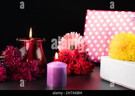 Fuoco selettivo su rosso decorativo o candela di cera di colonna di Maroon che si illuminano in lanterna del vetro del progettista. Bella fresca fiori colorati e Buca regalo Foto Stock